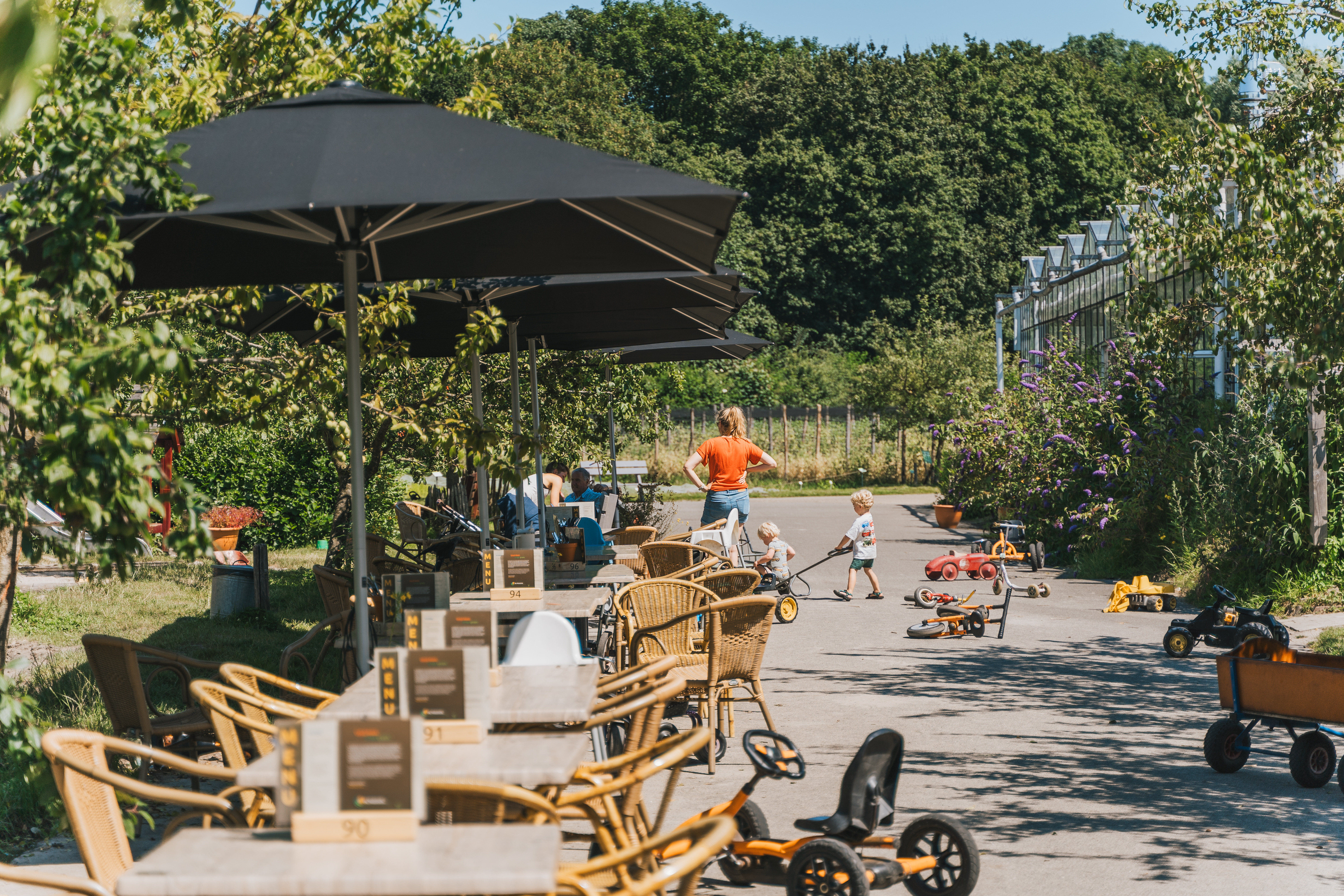 Terras met tafels en stoelen, skelter, bolderwagens en spelende kinderen 